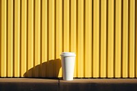 A white paper coffee cup onto a barricaded fence yellow wall architecture.