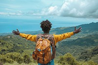Young Ethiopian man with backpack open arms in the mountains with view of ocean adventure outdoors nature.
