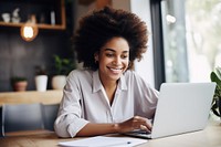 Black woman sitting at desk working on laptop computer smiling adult.