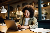 Black woman sitting at desk working on laptop computer smiling writing.