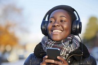 Happy young black woman holding mobile phone enjoying music listening through wireless headphones on footpath headset smile happy.