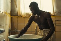 Black South African man bathroom cleaning bathtub.