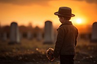 Sad little child boy in hat standing on cemetery at sunset tombstone outdoors adult.