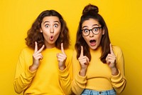Couple of young student girls surprised pointing glasses yellow.