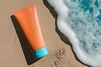 Orange sunscreen tube on sand