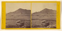 Long view of cabin on plain, rock formation at foreground by William Henry Jackson and Co