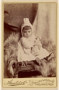 Baby girl in bonnet, seated, holding a doll by A Husted and Company