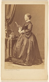 Unidentified woman, standing, looking at a book by Disdéri and Cie