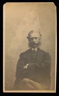 Unidentified man with muttonchops seated with arms crossed, a female "spirit" in the background by William H Mumler