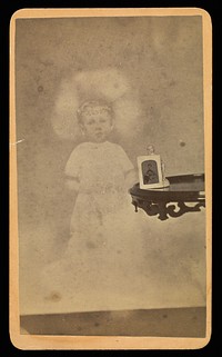 Child "spirit" with photograph and figurine on table by William H Mumler and Helen F Stuart
