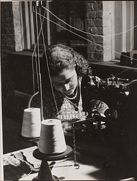 Woman uses a sewing machine threaded from two spools of white thread by Arnold Eagle