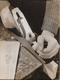 Man uses a wood plane with an instruction booklet sitting to the left by Arnold Eagle