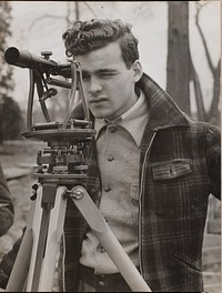 Young man peers through a surveyor's tool by Arnold Eagle