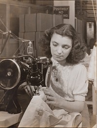 Woman wearing a heart-shaped necklace uses a sewing machine by Arnold Eagle