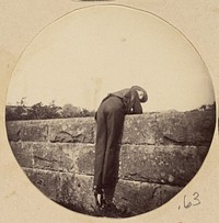 Man in hat bent over a stone wall