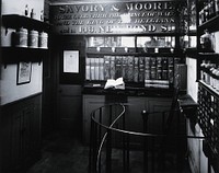 Savory & Moore Ltd: interior of the pharmacy; an upper floor which appears to be connected by a metal spiral staircase. Photograph.