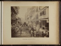 Groups of men on a street spraying jets of water into plague infected houses, during the epidemic of plague in Bombay. Photograph attributed to Captain C. Moss, 1897.