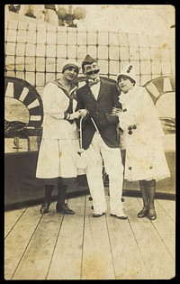Three sailors, two in drag wearing pierrette costumes, pose on deck. Photographic postcard, 191-.