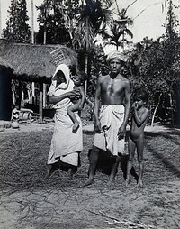 Assam, India: an Indian man and woman, wearing simple robes, with their two small children, outside a grass-roofed house. Photograph, 1900/1920 .