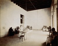 Waiting room in a dispensary for the treatment of tuberculosis, Cuba: a nurse stands beside the reception table, surrounded by seated patients. Photograph, 1902.