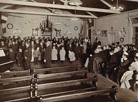 Metropolitan Lunatic Asylum, Kew, Victoria (Australia): patients, mostly children, entertaining some seated adults in a small wooden hall. Photograph.