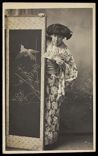 A man wearing a kimono posing from behind a screen.