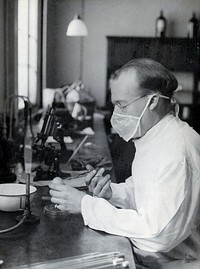Yellow fever: a scientist wearing a face mask works at a laboratory bench with bunsen burners and microscopes. Photograph, 1910/1930 .