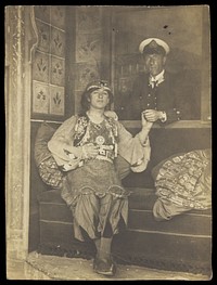 A sailor holds hands with a man in elaborate drag. Photographic postcard, 191-.