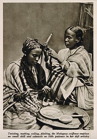 A Malagasy female hairdresser dressing the hair of a woman. Reproduction of a photograph.