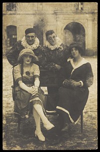 Members of 'The Stars' concert party, two soldiers in drag and two as pierrots, pose around a bench. Photographic postcard, 1919.