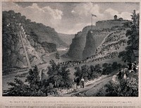 Crowds of people are standing on hillsides looking down on to a river in the valley over which the Clifton suspension bridge was to be built. Lithograph.