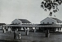 The Chandkuri Leper Home and Hospital, Baitalpur, India: two Indian women hold bowls on their heads in front of the hospital wards. Photograph, 1890/1910.