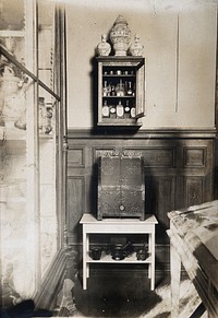 Some objects from the Musée Pharmacie: a small cabinet with pharmacy bottles and jars and a wooden box decorated with metal. Photograph.