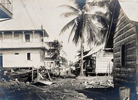 Colón, Panama: unpaved street with wooden houses and palm trees: building debris scattered in foregound; people visible in middle distance. Photograph, 1906.
