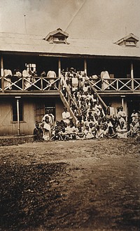 Accra, Ghana: African people waiting to be inoculated on the porch and steps of a (hospital) building. Photograph, 1910/1920.