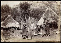 South Africa: Magwamba women grinding corn outside mud huts; one woman works with a baby in a fabric sling on her back. Photograph by H.F. Gros, ca. 1888.