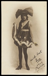 A man in drag poses wearing a short dress and large bow tie-shaped head garment. Photographic postcard, 192-.