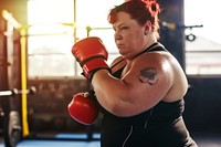 A chubby woman kickboxing in a bright gym to get a workout punching sports determination.