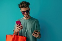 Smiling young man wear sunglasses using her smartphone red bag shopping bag.