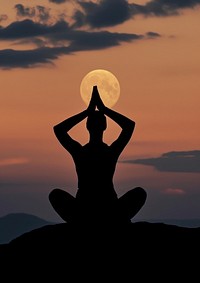A woman silhouette sitting put the hand together above the head or doing yoga on the mountain in front of the moon backlighting outdoors nature.