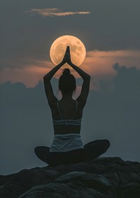 A woman silhouette sitting put the hand together above the head or doing yoga on the mountain in front of the moon astronomy outdoors nature.