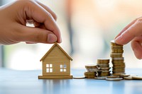 Photo of one hand presenting a miniature house to another hand with stack of coins money architecture investment.