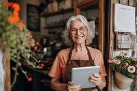 Senior woman holding tablet and standing at doorway of her coffee shop adult happy entrepreneur.