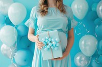 Woman holding present to give pregnant woman turquoise balloon party.