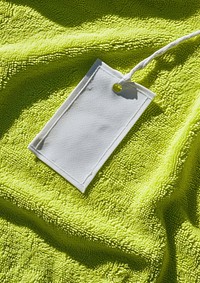 Empty white label tag printing sewn on flatlay flatten lime green open towel sunlight crumpled outdoors.