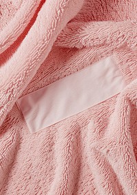 Empty white cotton long rectangle label vertical sewn on flatten pink towel backgrounds softness crumpled.