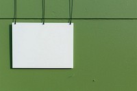 A business card is hanging on a black grid fence wall architecture green.