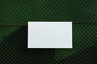 A business card is hanging on a black grid fence green paper backgrounds.