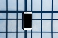 A smartphone is hanging on a black grid fence wall blue architecture.
