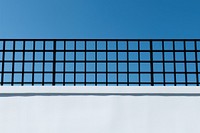 A black grid fence white wall blue.